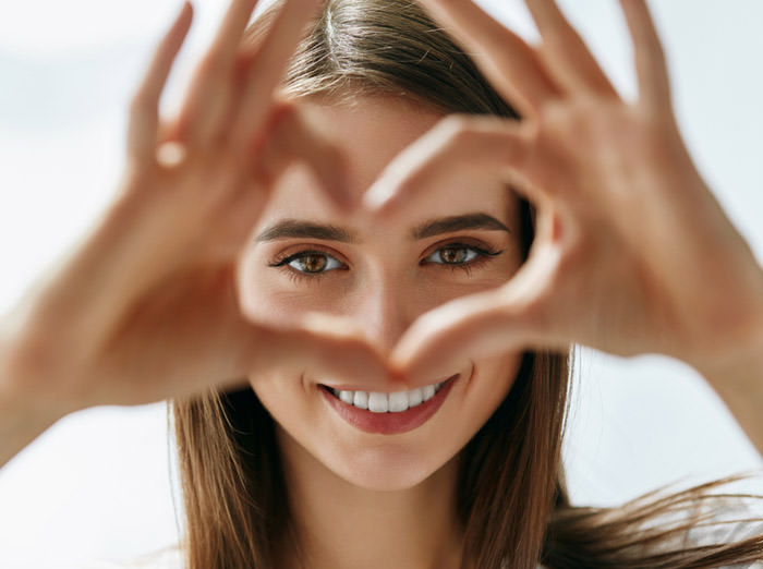 A woman looking at the camera through her hands shaped like a heart