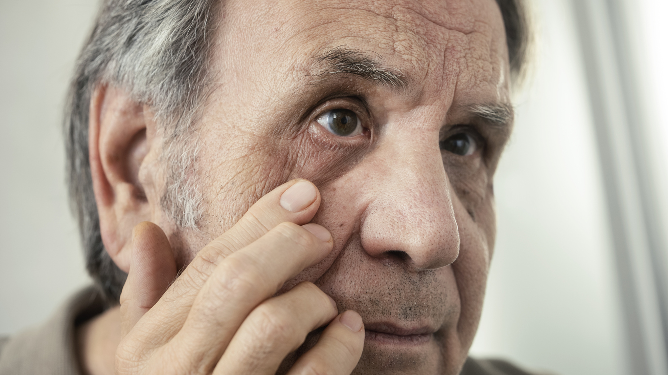 Old man examines his own eye in the mirror