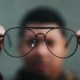 Glasses held close to the camera with a man's blurry face behind them