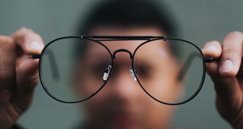 Glasses held close to the camera with a man's blurry face behind them