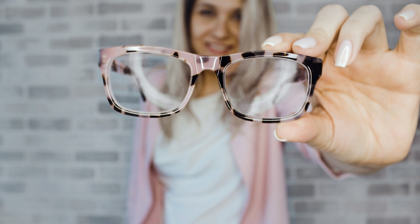 Woman holding glasses in front of Rockville, MD Eye Doctor office.