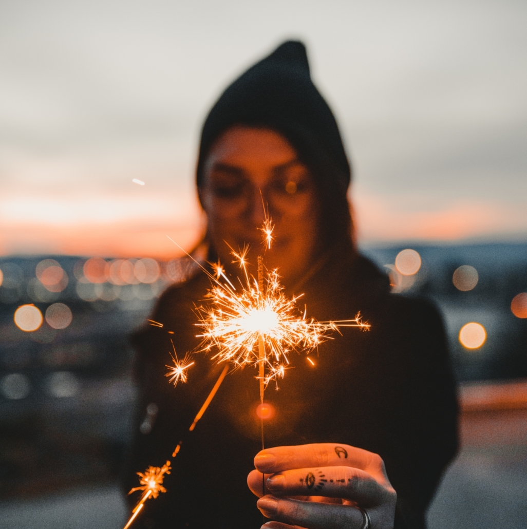 Woman in hoodie wearing glasses and playing with sparkler.