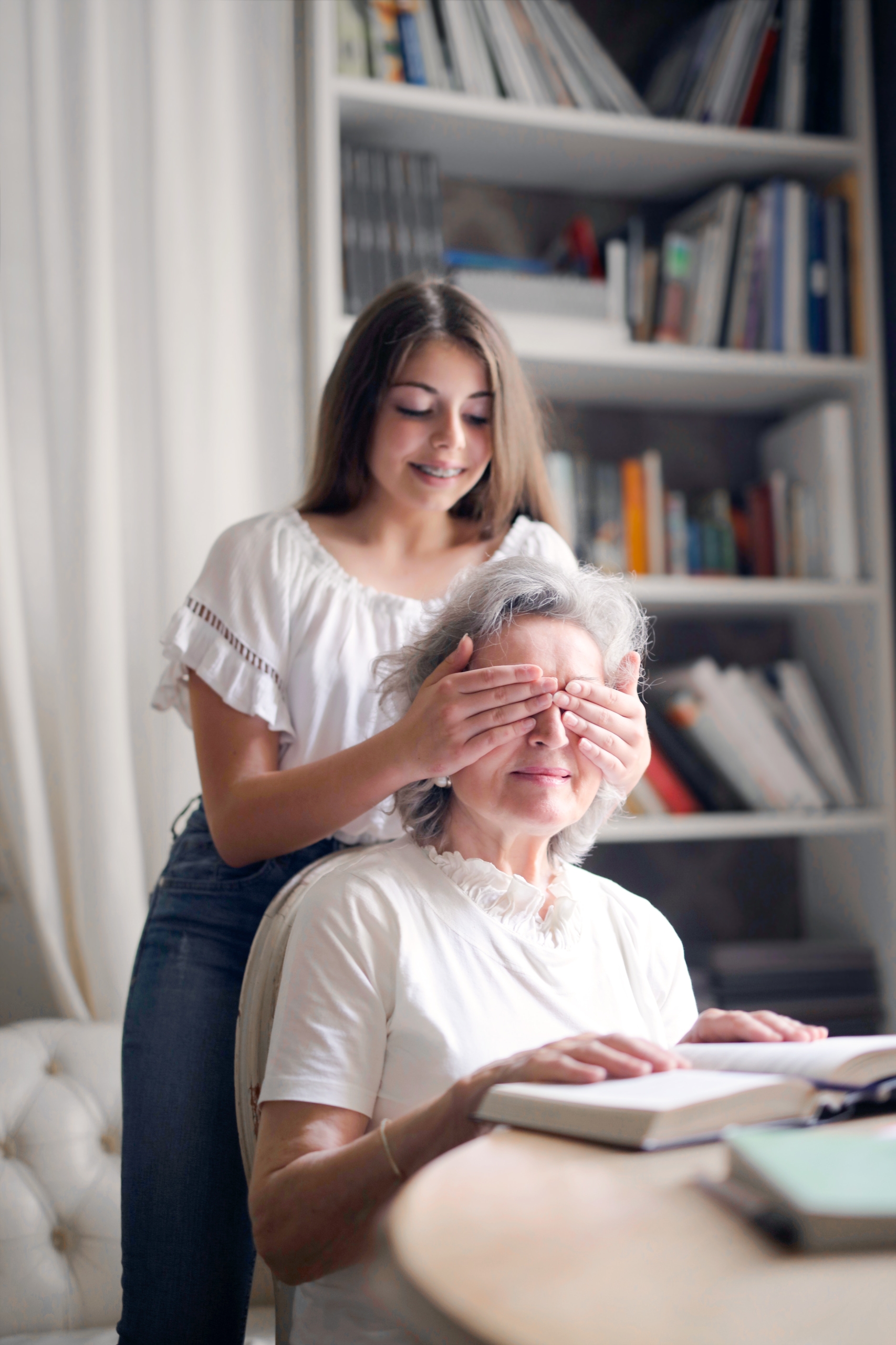 Young girl covering eyes of elderly grandmother in a library