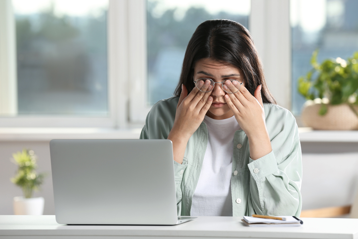 Young woman suffering from eyestrain at desk in office