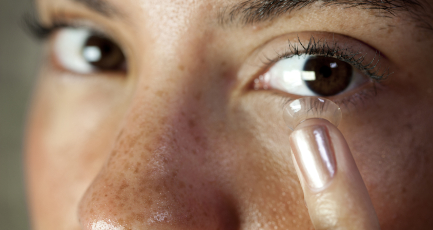 Eye contact from a woman inserting a contact lens into her eye. Macro focus on the lens and eyelash.