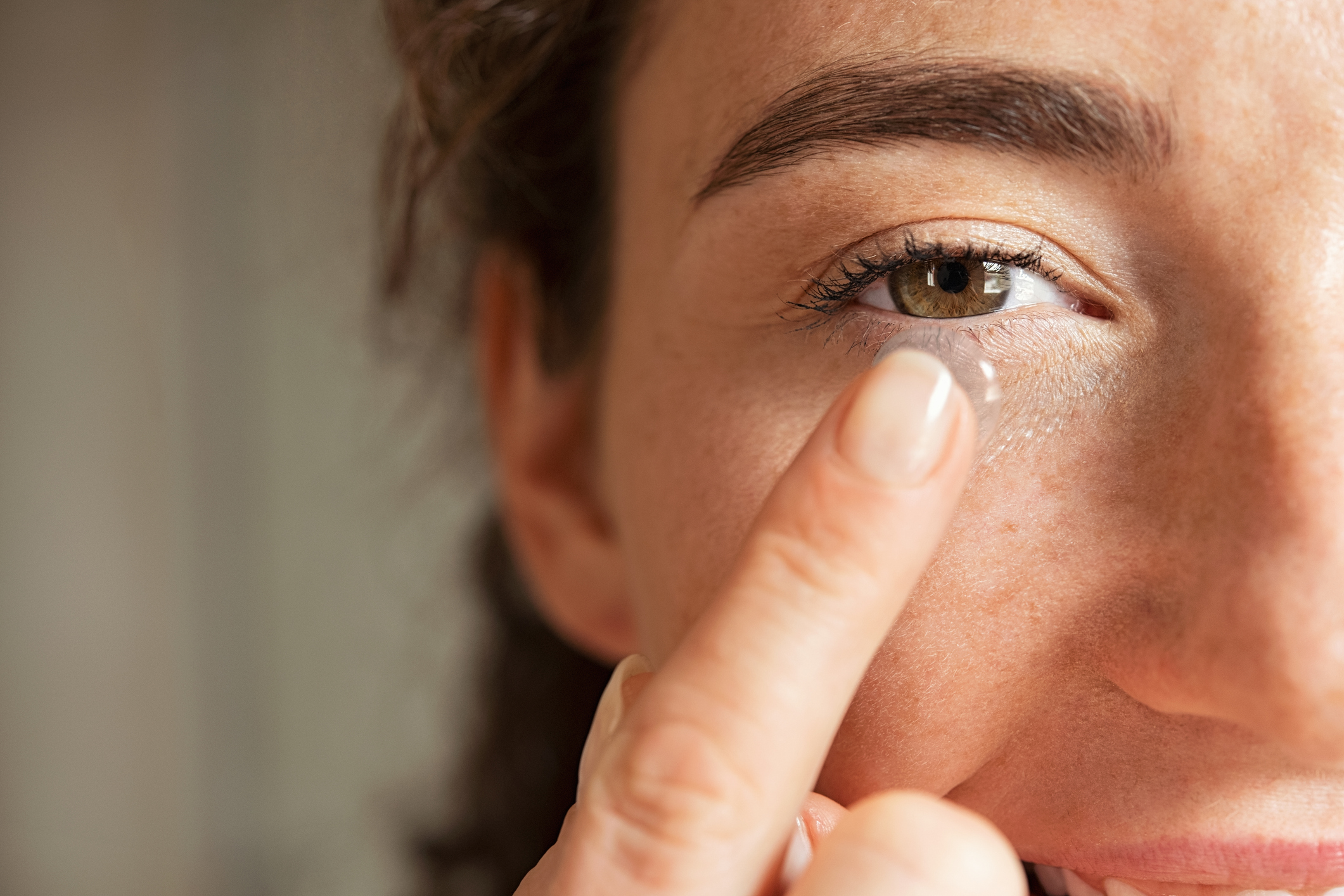 Close up of young woman wearing contact lens with copy space. Young woman holding transparent contact lens on index finger while looking at camera. Close up eye of healthy beautiful girl about to wear contact-lens.