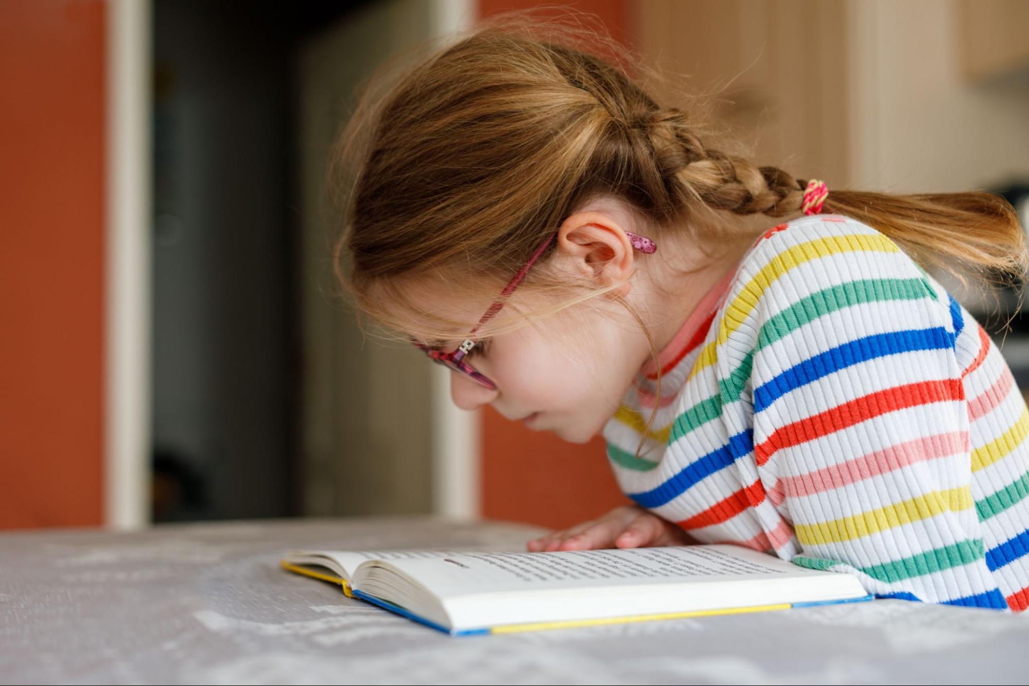 Young girl looking closely at book while wearing glasses